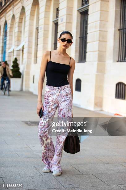 Vanessa Tyagi wears black sunglasses, a black camisole tank top, high-rise pink straight Etro paisley pants, white sneakers, a brown purse after the...