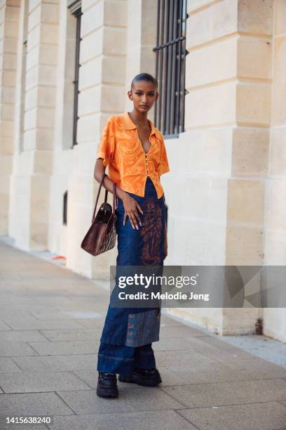 Model Camille Gilles wears an orange swirl print front button deep plunge shirt with collar, high rise long denim skirt over wide legged pants with...