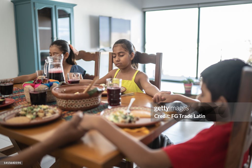 Mexican family praying before having lunch together in the dining room at home