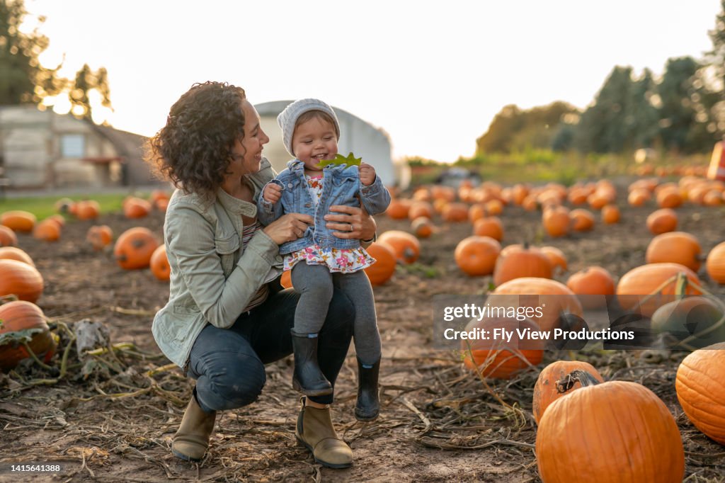 Mamá étnica de treinta y tantos levantando a su niño pequeño en el aire en un parche de calabaza