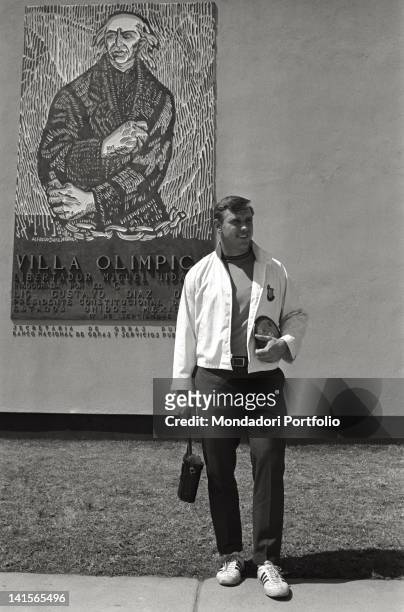 The US discus thrower Al Oerter at the Olympic Village. Already winner of three gold Olympic medals, he is posing in front of a reproduction of a...