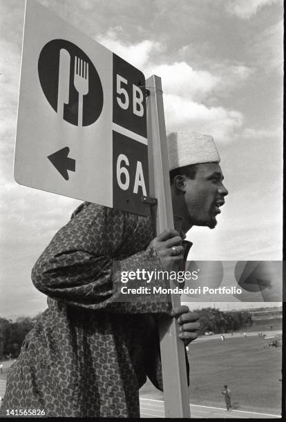 The US sprinter John Carlos, photographed in the Olympic Village of Mexico City, is leaning against a sign indicating how to reach the canteen....
