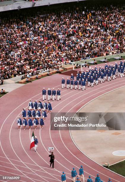 The team of Italian athletes participating to the Olympic Games is parading in the University Olympic Stadium. In front of the group, the flag...