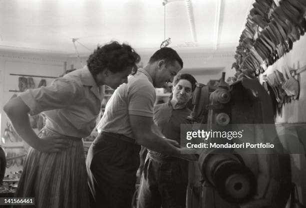 The Czechoslovakian discus thrower Olga Fikotova looking at her husband the American hammer thrower Harold Connolly trying a machinery in a shoe shop...