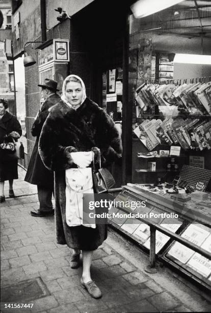 The Swedish actress Ingrid Berman walking passing in front of a newspaper kiosk. Stockholm, 1959