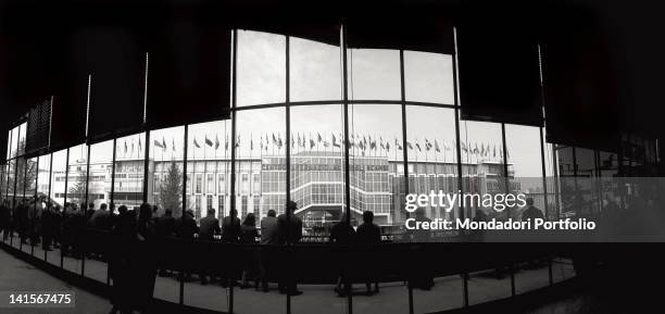 Visitors watching from the large windows of a building the front of the International Trade Centre . Milan, April 1965