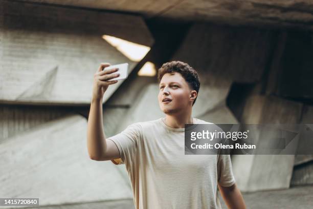 young man taking photo on mobile phone against wall. - man photographer stock pictures, royalty-free photos & images