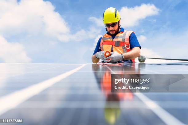 males engineer working in the high level to check the efficiency of solar photovoltaic panel and use full body harness protection suit against with blue sky. - service level high stock pictures, royalty-free photos & images