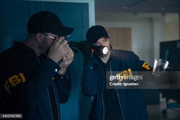 two fbi agents in uniform inspecting the crime scene in a dark room at the den of criminals, taking pictures of a glass, as physical evidence - military uniform close up stock pictures, royalty-free photos & images