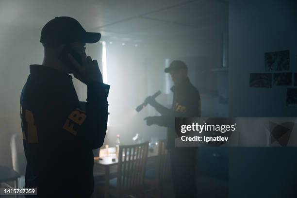 two fbi agents at the crime scene in a foggy room of the criminal's apartment, calling reinforcements on the phone - fbi warning stock pictures, royalty-free photos & images