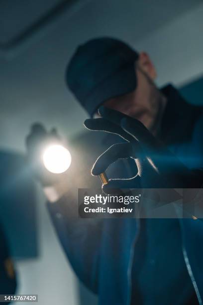 die hand eines fbi-agenten hält eine kugel, die er mit einer taschenlampe beleuchtet - leuchtgeschoss stock-fotos und bilder
