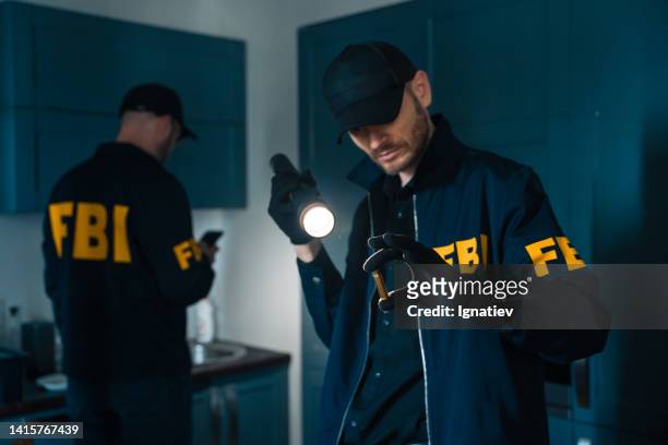 fbi-agenten in einem dunklen raum inspizieren eine kugel als physische beweismittel, die am tatort zurückgelassen wurde, und zünden sie mit einer taschenlampe an - leuchtgeschoss stock-fotos und bilder