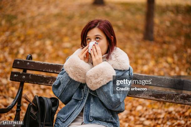 joven sonándose la nariz en el parque en otoño - sistema inmune humano fotografías e imágenes de stock