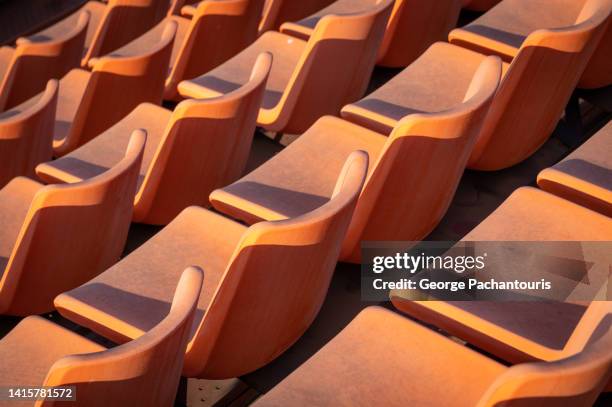 rows of orange seats at an outdoors theater - silla vacía fotografías e imágenes de stock