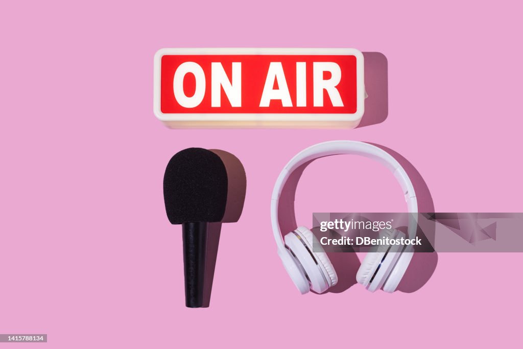 Lightbox turned on with the word 'On air', headphones and microphone with windscreen on pink background. Concept of radio, podcast, streaming, broadcast, journalism, reporting and shows.