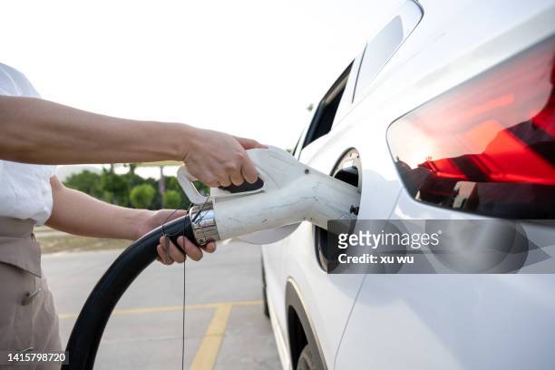 woman holding socket and charging at car charging station - charge stockfoto's en -beelden