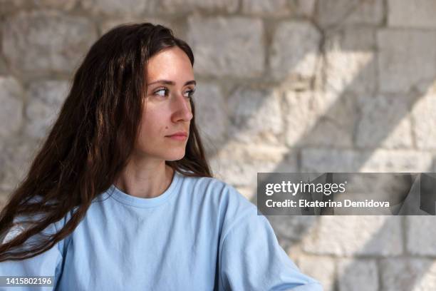 uncertain woman looking away suspiciously against brick wall - jaloezie negatieve emotie stockfoto's en -beelden