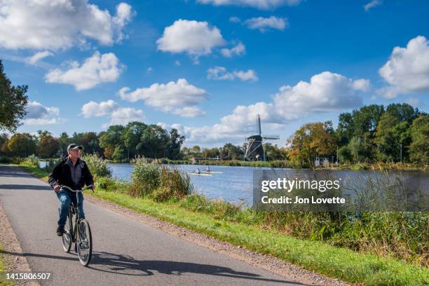 cyclist on the amstel river with rieker windmill in background - fluss amstel stock-fotos und bilder