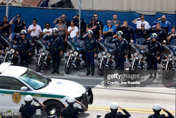 Police officers salute as a Miami-Dade Fire Rescue truck carries the casket of Miami-Dade Detective Cesar Echaverry during a honor procession to the...