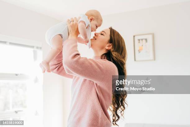 young mother with raised arms holding baby close to face in living room - mothers babies stockfoto's en -beelden