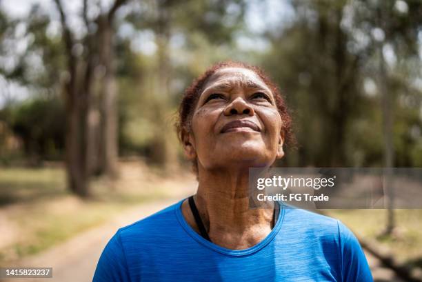 contemplative senior woman looking up in a park - zichtbare adem stockfoto's en -beelden