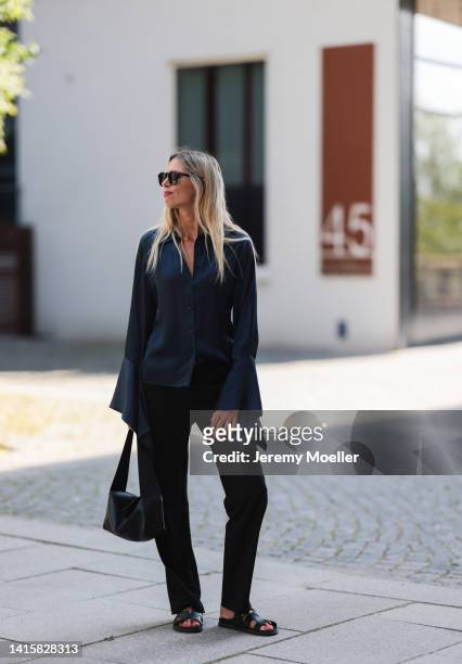 Vanessa Giers is seen wearing a black Loewe bag, black Hermes Chypre sandals, Tom Ford shades, SoSue navy blue silk blouse and black SoSue pants on...