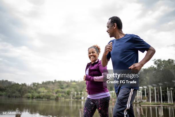 pareja mayor trotando en un parque - active lifestyle fotografías e imágenes de stock