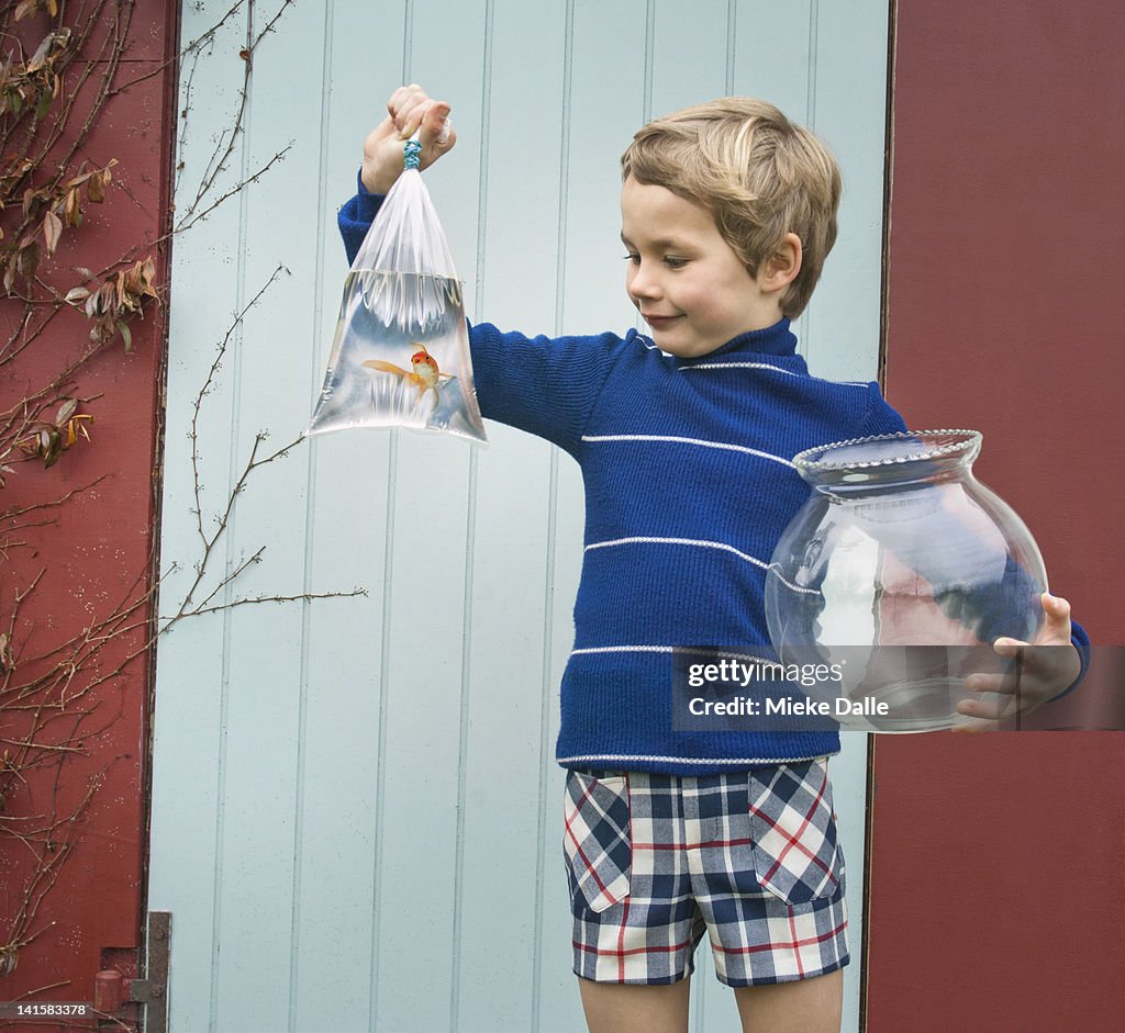 Child holding  bowl and goldfish in a plastic bag