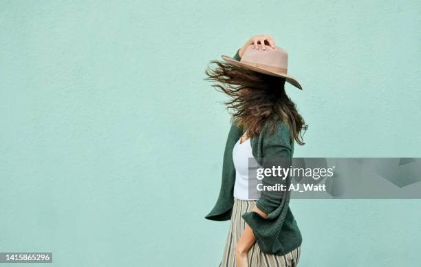 vista lateral de una mujer joven sosteniendo su sombrero en la brisa - mint green fotografías e imágenes de stock