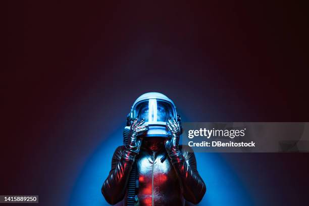 astronaut cosmonaut dressed in a gold jumpsuit and helmet, illuminated by blue and red lights, with his hands on the case and looking up. concept of exploration, space, planet, strange and alien. - science et technologie stock-fotos und bilder