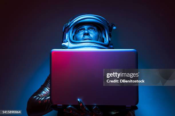 close shot of cosmonaut astronaut dressed in a gold jumpsuit and helmet, illuminated by blue and red lights, holding a laptop, looking up. concept of exploration, space, planet, strange and alien. - blue jumpsuit foto e immagini stock