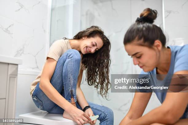 smiling female cutting toenails with girlfriend in bathroom - teen lesbian stockfoto's en -beelden