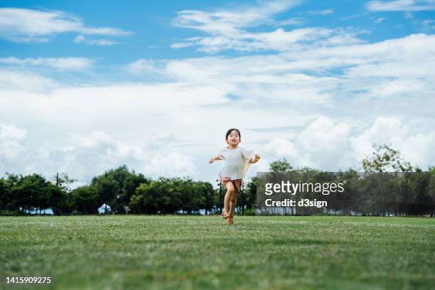 happy little asian girl having fun running on lawn in the park against beautiful blue sky. enjoying nature and summer days outdoors. childhood lifestyle, carefree and freedom concept - public park kids stock pictures, royalty-free photos & images