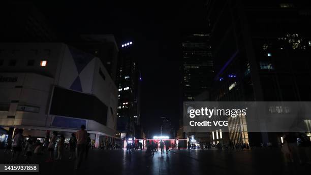 People walk in the darkness at the Chunxi Road pedestrianized shopping street as many lights are switched off to conserve energy on August 19, 2022...