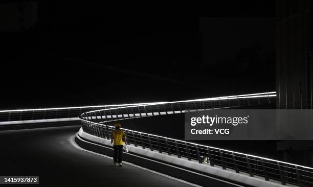 Meituan food courier walks in the darkness at the Chunxi Road pedestrianized shopping street as many lights are switched off to conserve energy on...