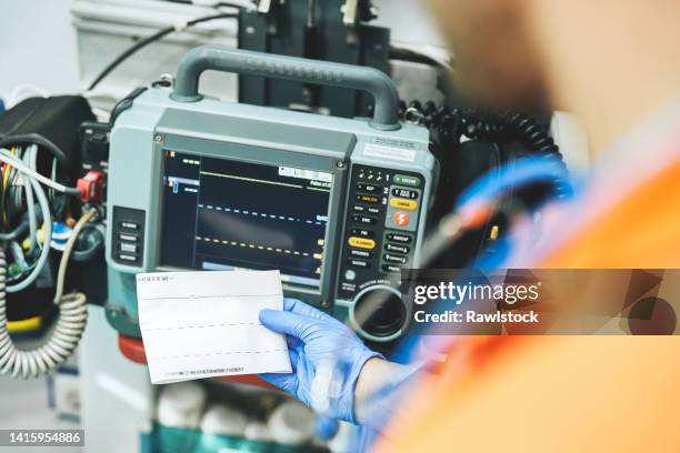 paramedic holding an electrocardiogram next to a defibrillator monitor in an ambulance - desfibrilador fotografías e imágenes de stock