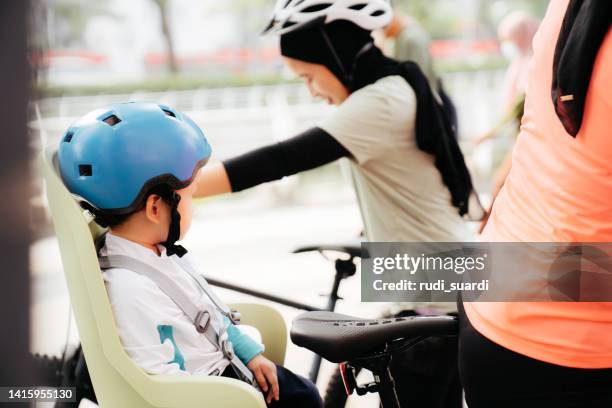 zwei muslimische frauen fahren fahrrad in der stadt und das baby sitzt auf dem rücken - baby sturzhelm stock-fotos und bilder