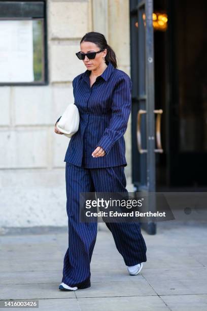 Guest wears black sunglasses, gold earrings, a navy blue striped print pattern belted blazer jacket, matching navy blue striped print pattern large...