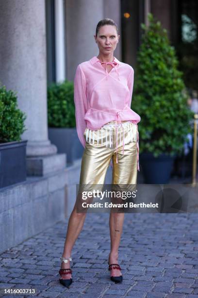 Guest wears a pale pink linen laces shirt, gold shiny leather shorts, black satin with a red pearls strap pumps heels slingback shoes, outside Saks...