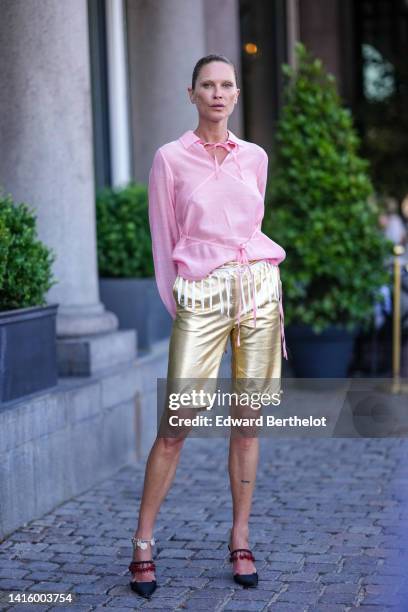 Guest wears a pale pink linen laces shirt, gold shiny leather shorts, black satin with a red pearls strap pumps heels slingback shoes, outside Saks...