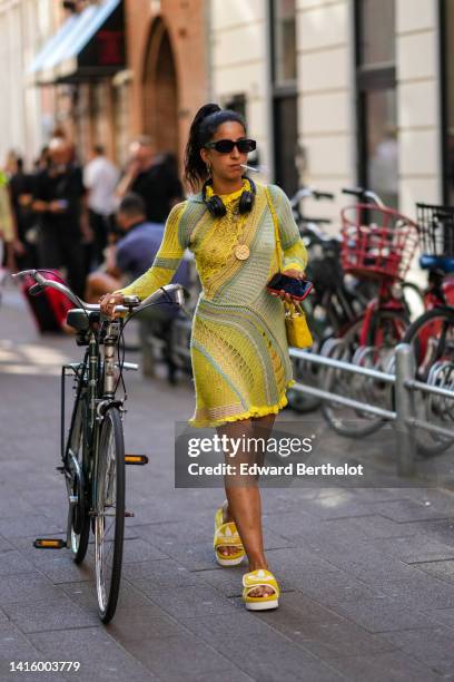 Guest wears black sunglasses, gold earrings, a black headphones, a yellow and pale gray braided / ripped long sleeves / ruffled high neck / short...