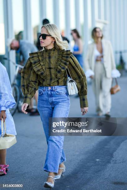 Guest wears black sunglasses, silver earrings, a khaki and black checkered print pattern / ruffled collar / puffy long sleeves blouse / shirt, white...