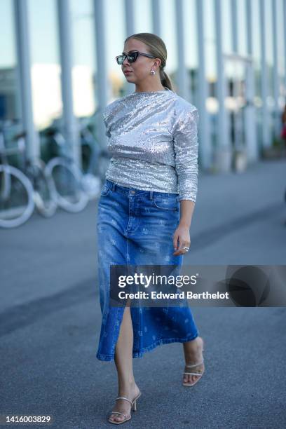 Guest wears black sunglasses, silver earrings, a silver shiny sequined long sleeves / shoulder-pads t-shirt, blue denim with embroidered logo print...