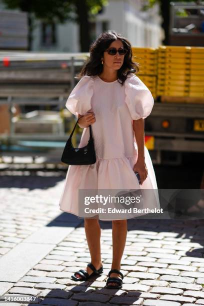 Guest wears black sunglasses, gold earrings, a white puffy short sleeves / ruffled knees dress, a black nylon handbag from Prada, black shiny leather...