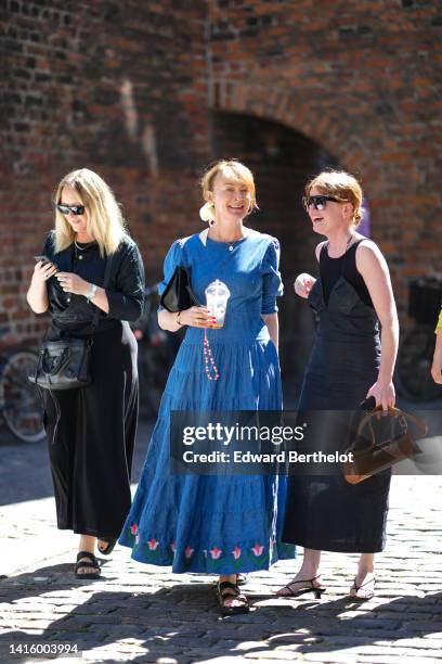 Guest wears black sunglasses, a black long sleeves t-shirt, a black long dress, a black shiny leather City crossbody bag from Balenciaga, black...