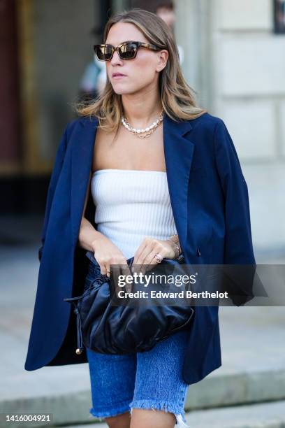 Guest wears black sunglasses, a white pearls necklace, a gold chain necklace, a white ribbed wool shoulder-off top, a navy blue oversized blazer...