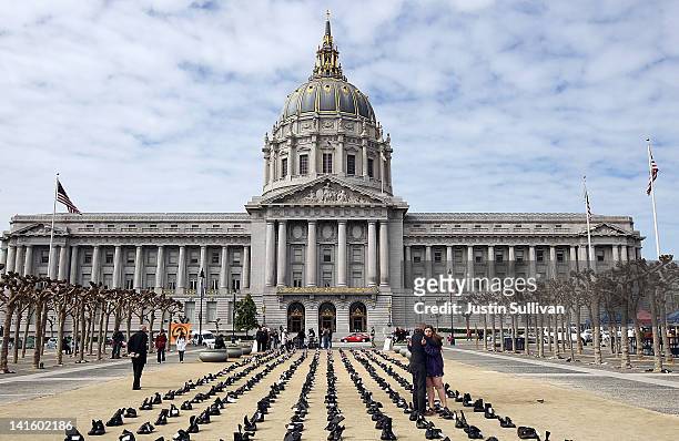 People embrace as they stand among rows of combat boots that are part of the "Eyes Wide Open" exhibit in front of San Francisco City Hall on March...