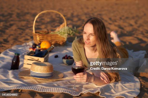 a beautiful woman on the sandy shore on a picnic blanket with a wineglass with red wine. - picnic rug stockfoto's en -beelden