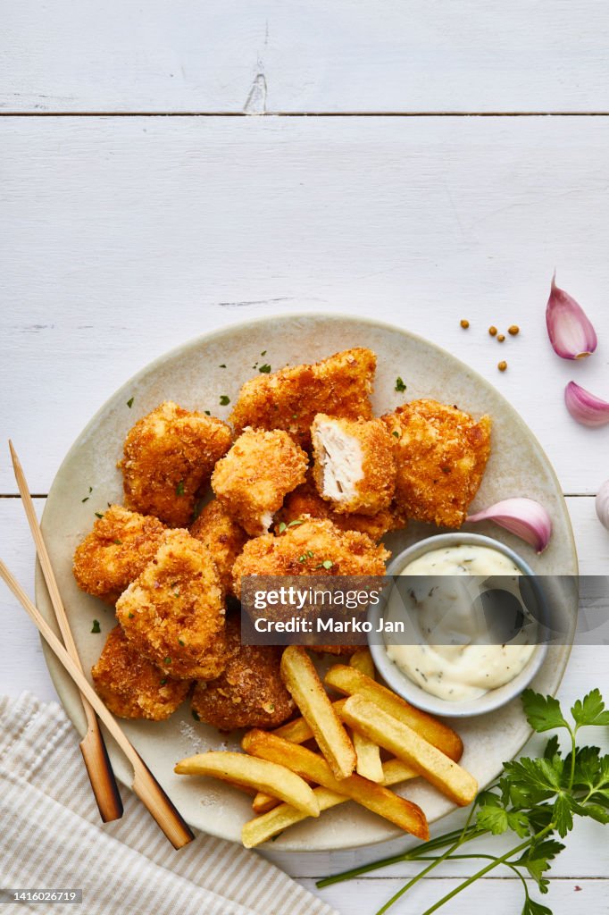 Tasty chicken nuggets on a plate, with french fries and white sauce
