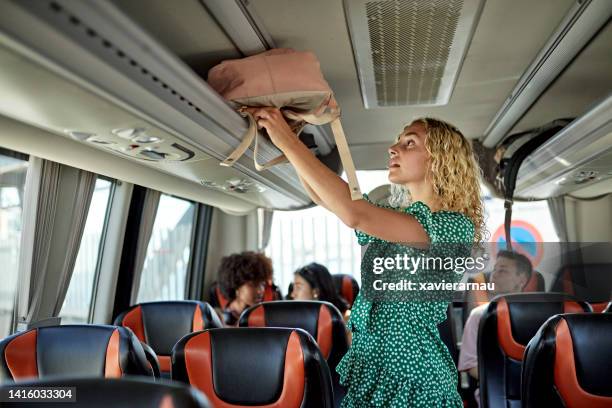 teenage girl stowing bag in coach luggage rack - luggage rack bildbanksfoton och bilder